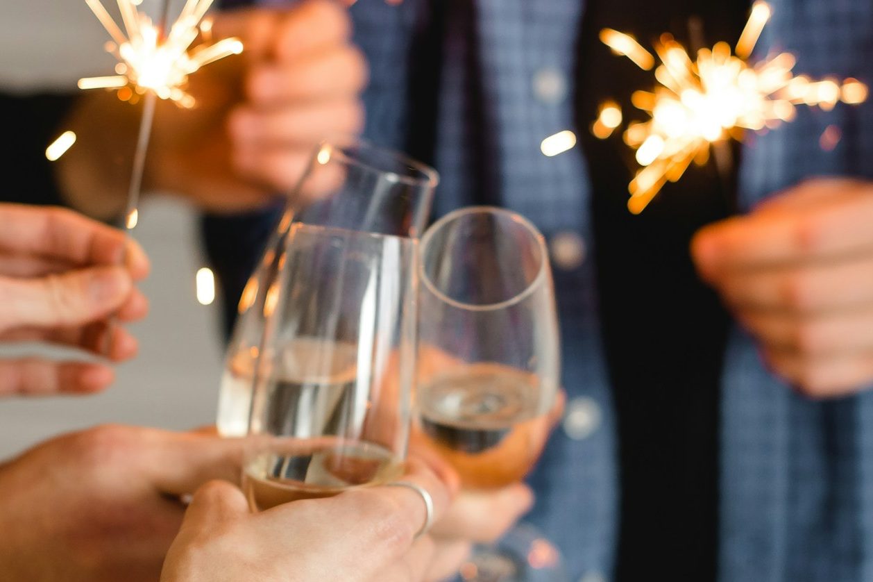 Hände stoßen mit Sekt-Gläsern an und halten Wunderkerzen.
