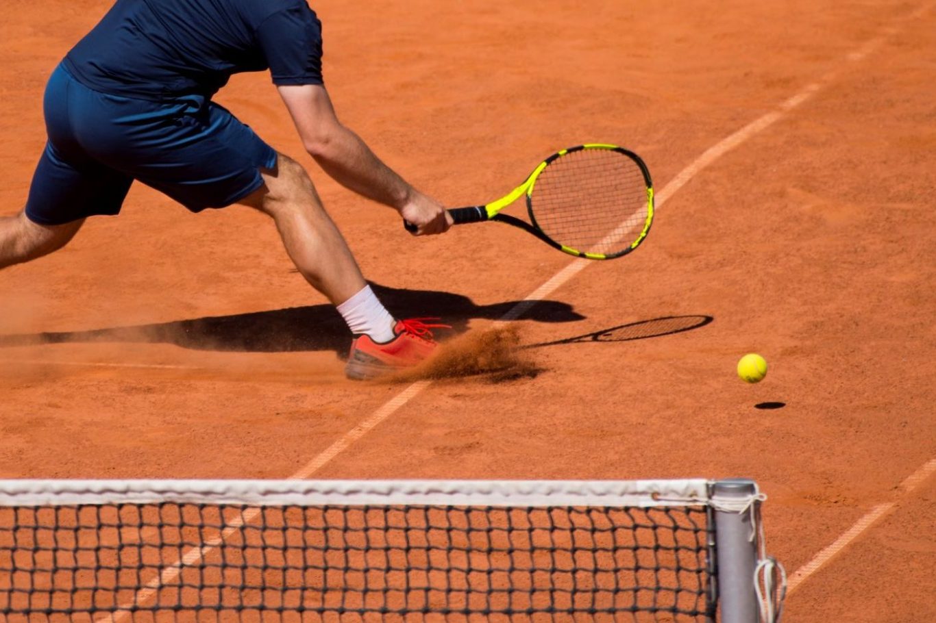 Tennisspieler schlägt den Ball auf einem Sandplatz.