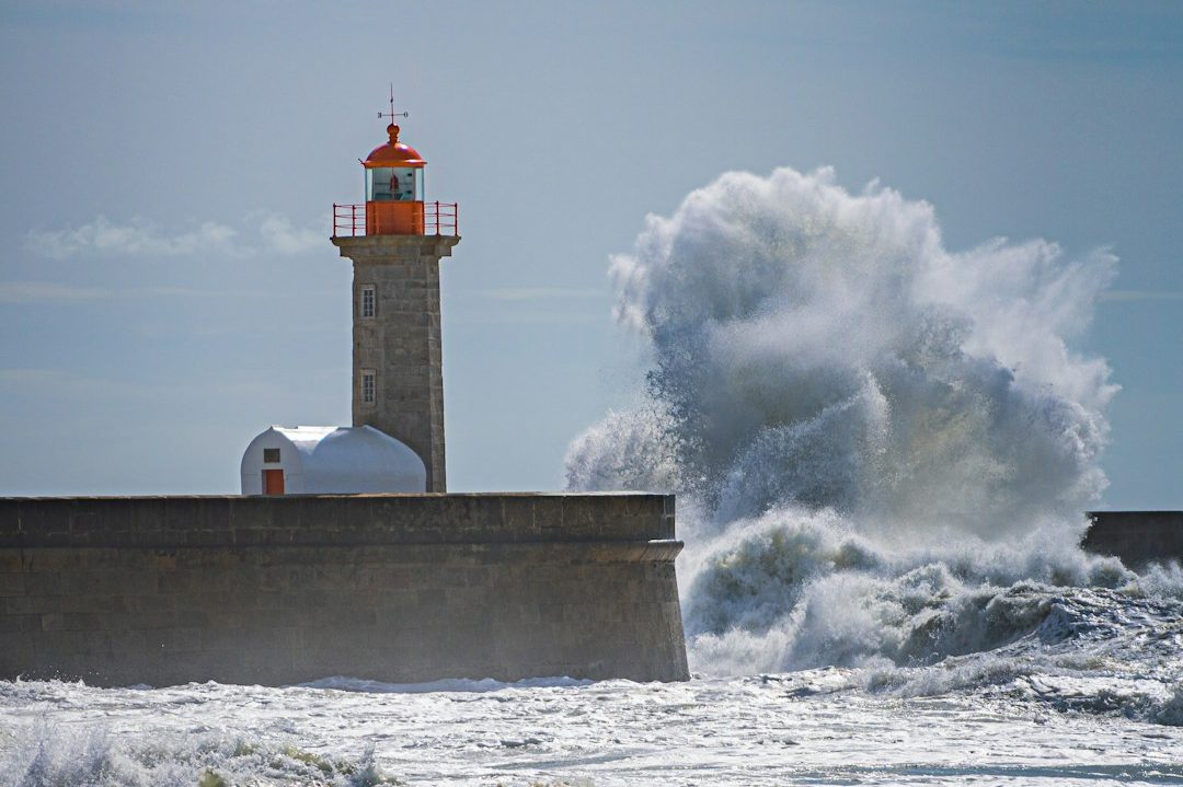 Leuchtturm an der Küste mit großen, aufspritzenden Wellen, die auf den Leuchtturm wehen.